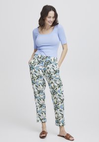 Ljusblå, figursydd topp med korta ärmar, tillsammans med vita byxor med blommönster i gröna och blå nyanser. Bruna platta sandaler.