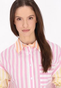 Camicia a righe con colori rosa, giallo e arancione. Materiale in cotone con bottoni sul davanti e tasca sul petto. Collo pieghevole.