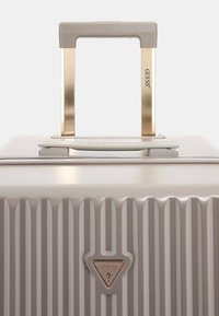 Valigia beige chiaro con righe verticali, finitura lucida, manico in metallo dorato e accentuazione del logo dorato. Design compatto per i viaggi.