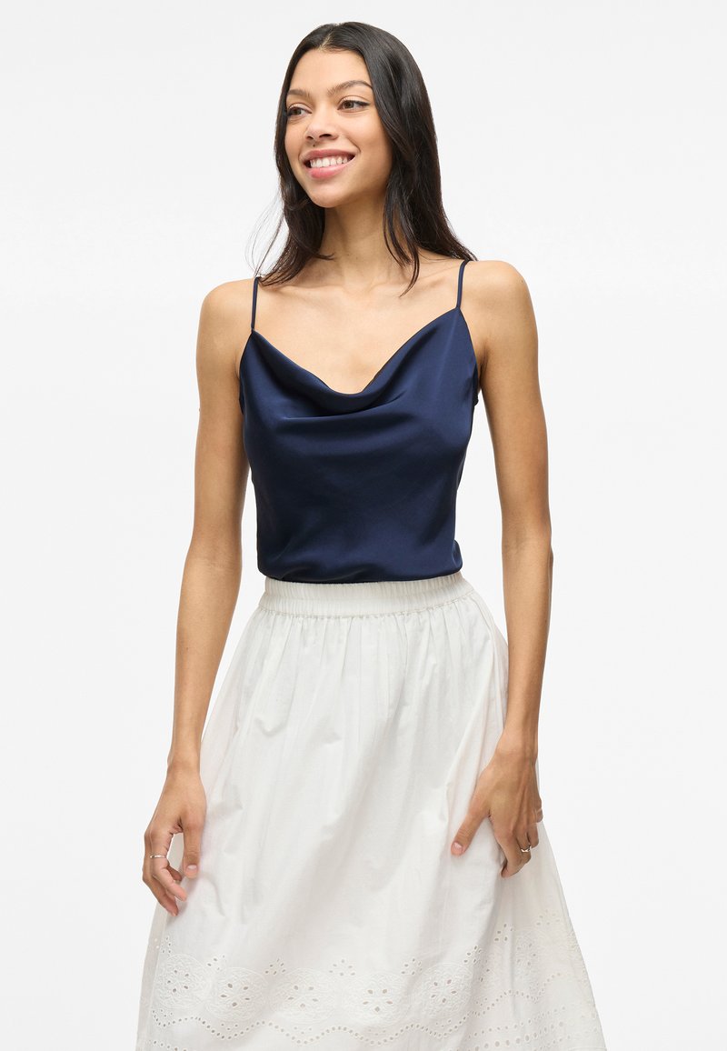 Navy Satin-Camisole mit Cowl-Ausschnitt und dünnen Trägern, kombiniert mit einem weißen bestickten A-Linien-Rock mit gerafftem Taillenbund.