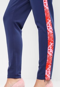 Marinblå byxor med sidopanel som har ett virvlande mönster i rosa och rött, slim fit, och med dragkedjor vid anklarna.