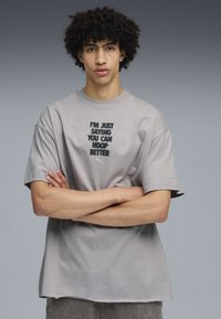 Camiseta de algodón gris con mangas cortas, con un diseño de texto en negro: "SOLO DIGO QUE PUEDES JUGAR MEJOR" y un pequeño logo.