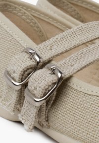 Chaussure en toile beige clair avec une texture tissée, dotée de boucles en métal argenté et de sangles pour l'ajustement. Design traditionnel avec des accents cousus.