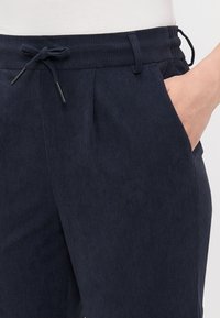 Marineblauwe corduroy broek met een gestructureerde afwerking, voorzien van een elastische tailleband met een trekkoord, voorzakken en taps toelopende benen.