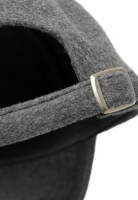 Casquette de baseball en laine grise montrant un gros plan de la sangle réglable avec boucle métallique argentée sur fond blanc.