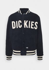 Giacca in pile di colore blu navy con lettering "DIC KIES" in crema. Presenta polsini e orlo a coste con righe, chiusura a bottoni e tasche laterali.