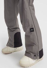 Grijze waterdichte broek met een zwart textuur paneel bij de enkel, voorzien van een logo patch en een veelzijdig design. Gepaard met off-white sneakers.