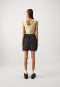 Halenka bez rukávů s vlněným výstřihem v béžové barvě, doplněná černými šortkami s elastickým pasem. Modelka nosí hnědé platformové boty a bílé ponožky.