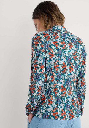 Blusa a maniche lunghe in teal con stampa floreale rossa, bianca e viola. Presenta un collo a camicia e una texture arricciata sul retro.