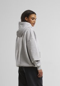 Grau übergroßer Hoodie mit großer Kapuze, überschnittenen Schultern, gerippten Bündchen und einer Kängurutasche. Weicher, strukturierter Stoff.
