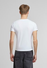 Hvit bomulls t-skjorte med korte ermer, rund hals og tettsittende snitt, kombinert med mørkegrå jeans med to baklommer.