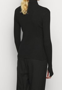 Svart ribbad polotröja med långa ärmar; tät passform; texturerad tyg; bakifrån syns en något utsvängd fåll.
