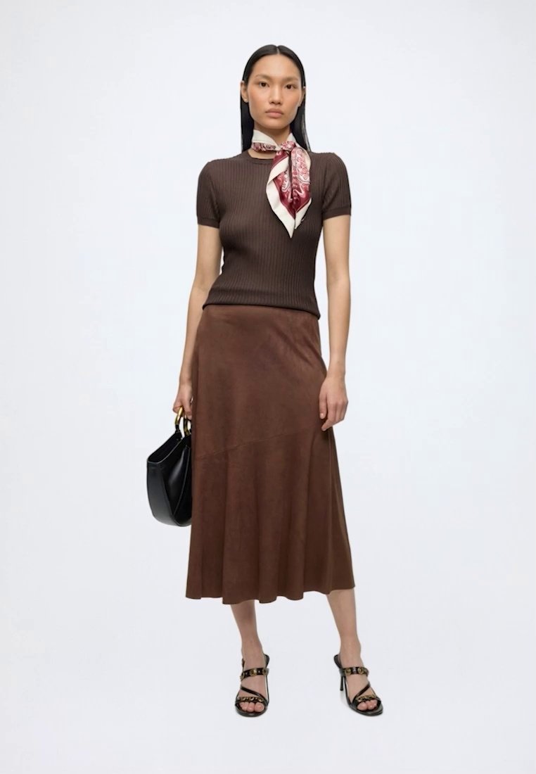 Femme portant un haut marron côtelé à manches courtes, une jupe midi marron, une écharpe à motifs, des sandales noires à talons hauts, et tenant un sac à main noir.