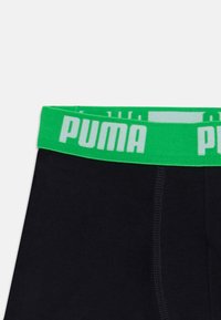 Črne bokserice z svetlo zelenim pasom, ki vsebuje belo oznako "PUMA". Gladka tekstura tkanine in standardna zasnova.