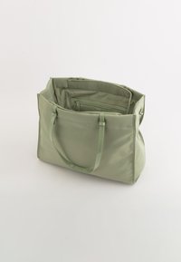 Grön nylonhandväska med två handtag, dragkedjestängning och inre fack, har en slät yta och rena linjer.