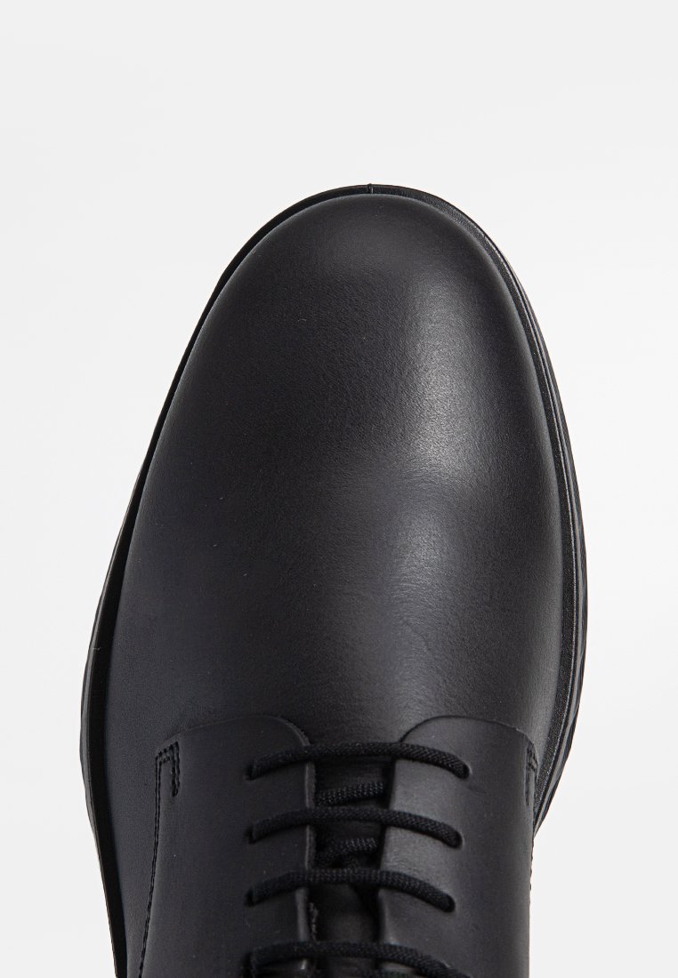 Schwarze Lederschuhe mit runder Zehe, minimalen Nähten und schwarzen Schnürsenkeln. Texturierte Oberfläche, glatte Verarbeitung und eine robuste Sohle.