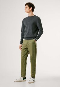 Pull en tricot gris foncé, chinos vert olive et baskets blanches avec des accents verts. Le pull a des poignets et un ourlet côtelés. Les chinos sont de coupe droite.