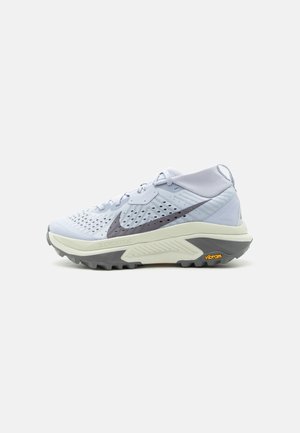 Világosszürke magas szárú futócipő fekete Nike logóval, hálós felsőrésszel, párnázott talppal és Vibram bordázott talpbetéttel.