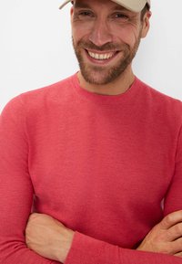 Roter Strickpullover mit rundem Ausschnitt und langen Ärmeln, der über ein strukturiertes Muster verfügt. Glattes Material, taillierte Passform und gerippte Bündchen.