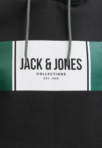 Schwarzer Kapuzenpullover mit einem weißen rechteckigen Grafikdesign und grünen Akzenten. Der Text lautet "JACK & JONES COLLECTIONS EST. 1990." Kordelzug mit gemustertem Detail.