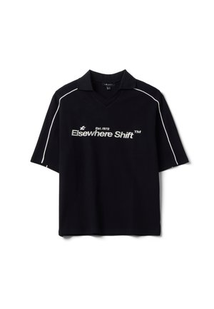 Polo nera a maniche corte con piping bianco sulle spalle e testo "Elsewhere Shift Est. 1972" stampato in bianco sul davanti.