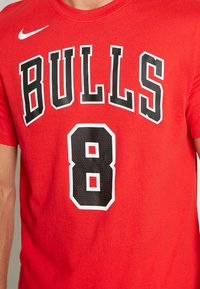 Rotes Baumwoll-T-Shirt mit der Aufschrift "BULLS" in fetten schwarzen Buchstaben und der Zahl "8" in einem schwarzen, perforierten Design mit weißen Umrissen.