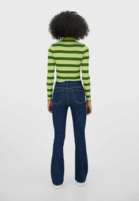 Zielono-biały prążkowany top w paski zestawiony z ciemnoniebieskimi rozkloszowanymi dżinsami. Top ma długie rękawy i wysoki kołnierz, a dżinsy posiadają tylne kieszenie.