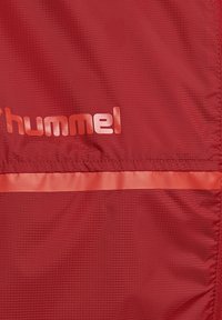Rood gestructureerde stof met een horizontale glanzende streep en gedeeltelijke "hummel" merklogo in glanzende letters.