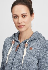 Felpa con zip in maglia blu a tonalità sfumata, caratterizzata da lacci crema con accenti in pelle marrone. Presente il cappuccio e il design con zip frontale.