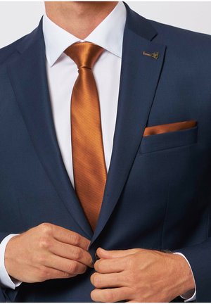 Marine-blau maßgeschneiderter Anzug aus strukturiertem Stoff, orangefarbene Satin-Krawatte und passendes Einstecktuch. Verfügt über eine kleine Markenbrosche am Revers.