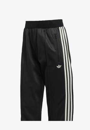 Pantalon de sport noir avec une ceinture côtelée, comportant trois bandes verticales blanches sur les côtés et une poche zippée sur la cuisse gauche.