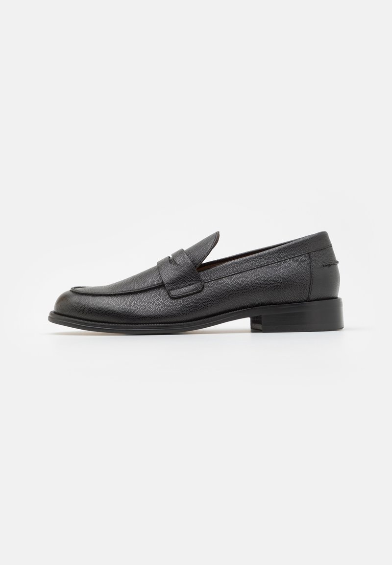 Mocassin homme en cuir noir avec petit talon et une bride sur le dessus, présenté de côté sur fond blanc.