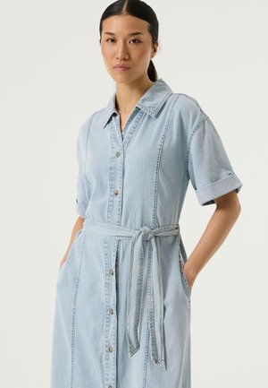 Hellblaues Denimkleid mit kurzen aufgerollten Ärmeln, Knopfleiste vorne, tailliertem Gürtel und Seitentaschen. Verfügt über sichtbare Nähte für zusätzliche Details.