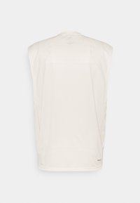 Beżowy bezrękawnik sportowy wykonany z miękkiego materiału o gładkiej teksturze, z okrągłym dekoltem i subtelnym logo na krawędzi.