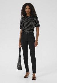 Black, fitted trousers with a button closure and front pockets, paired with a black and white striped short-sleeve top. Smooth fabric.