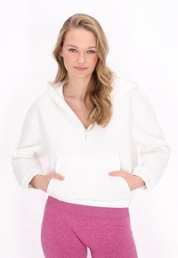 Vit zip-up hoodie med stor huva och framficka; mjuk textur, lös passform och muddade ärmar; matchad med rosa leggings.
