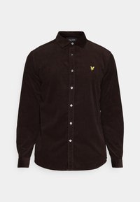 Camisa de pana marrón con mangas largas, cuello abotonado y botones blancos. Presenta un pequeño logo amarillo bordado en el pecho.