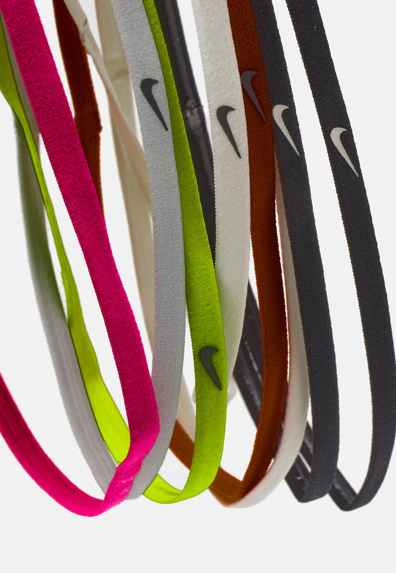 Sept bandeaux Nike de couleurs variées : rose, gris, blanc, vert, orange, noir et marron, fabriqués en matériau doux et texturé avec des accents du logo.