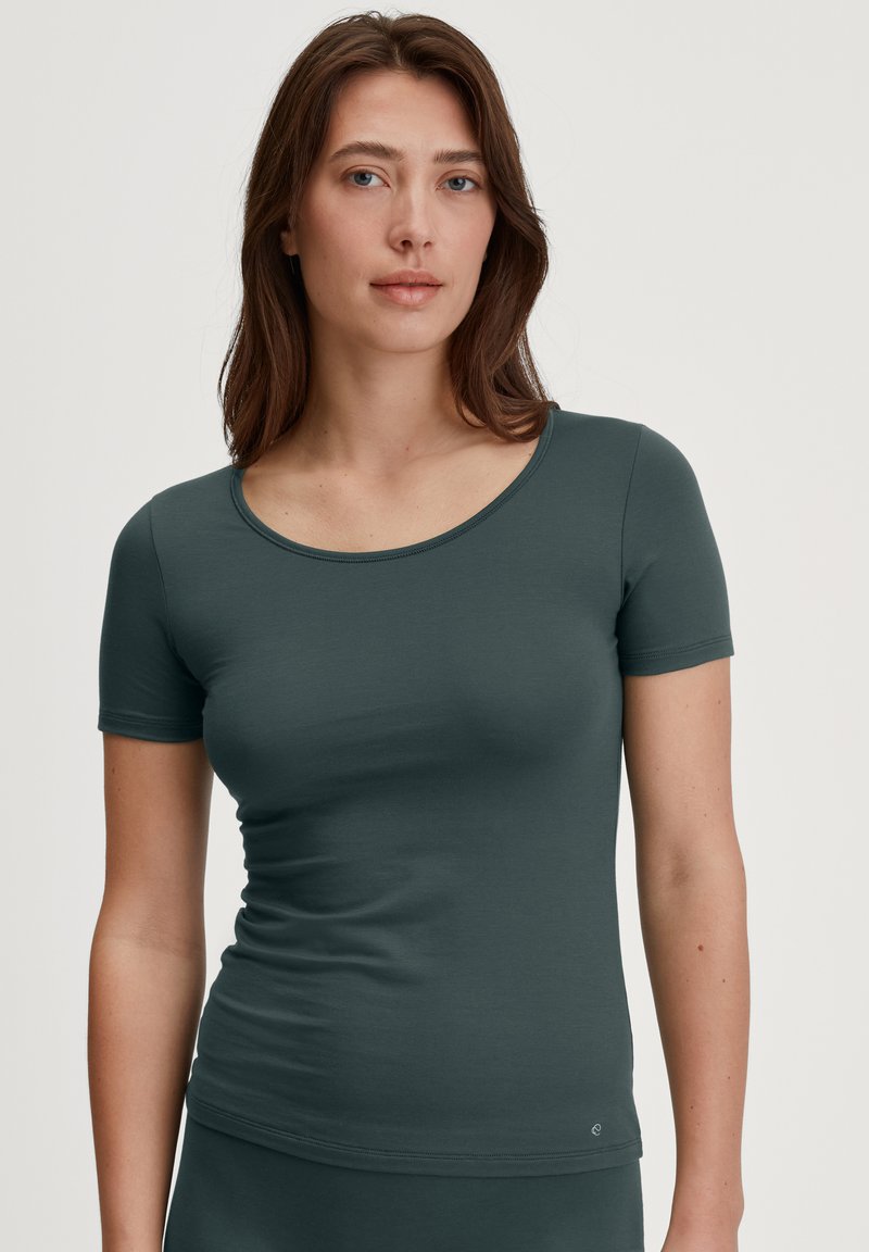 Top verde scuro a maniche corte con scollatura rotonda. Realizzato in un tessuto morbido e liscio, presenta una silhouette aderente e dettagli di cucitura minimi.