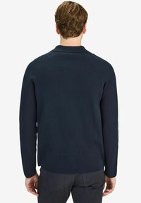 Navy blue, ribbed knit sweater with long sleeves and a round neckline, featuring a subtle texture and a relaxed fit.