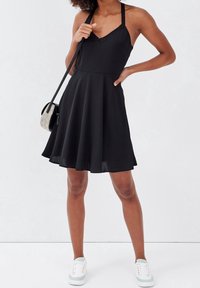 Black sleeveless dress with a V-neck and lace accents, fitted bodice, flared skirt, and paired with white sneakers.