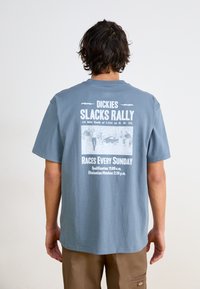 Pilkas medvilnės marškinėliai su trumpomis rankovėmis ir apvaliu kaklu. Nugarinėje pusėje yra balti užrašai ir grafika, susijusi su lenktynių renginiu.