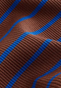 Gros plan d’un tissu brun côtelé avec des rayures verticales bleu vif espacées régulièrement, montrant la texture et de légers plis.