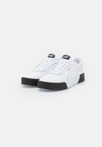 Bílé tenisky s černými gumovými podrážkami, vyrobené z hladké kůže, se šněrováním a drobnými zlatými logy.