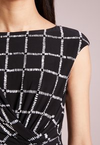 Black dress with a white grid pattern, featuring short sleeves and a twisted waist detail, made from a smooth, lightweight fabric.