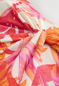 Tissu torsadé au centre avec des motifs floraux tropicaux orange et roses sur fond blanc.