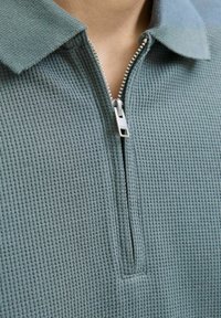 Lichtblauwe textuur quarter-zip pullover met ribbelstof, een puntige kraag en een zilveren rits met een stoffen trekband.