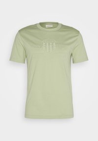 T-shirt en coton vert clair à manches courtes, avec un logo "GANT" en relief et le texte "AMERICAN SPORTSWEAR" sur le devant.