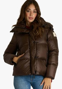 Giacca a vento marrone con texture lucida, collo alto e tasche con cerniera. Presenta chiusura con bottoni e design trapuntato per l'isolamento.