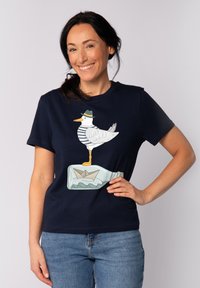 Navy-Blaues Baumwoll-T-Shirt mit einem Grafikdesign eines Möwen in gestreiftem Hemd und Hut, die auf einer Flasche mit einem Papierboot darin steht.